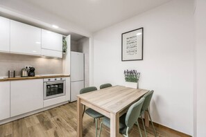 A modern kitchen with white cabinets, a wooden countertop, a built-in oven, and a dining area with a wooden table and green chairs. - Bright Modern Home with Terrace (Madrid)