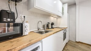 Une cuisine moderne avec des meubles blancs, un plan de travail en bois, un lave-vaisselle encastré, un four à micro-ondes, une bouilloire et un évier.