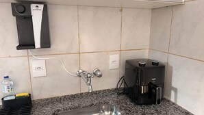 A kitchen with a stainless steel sink, a coffee maker, and a water dispenser. - Private studio apartment with Smart TV and air conditioning. (Belo Horizonte)