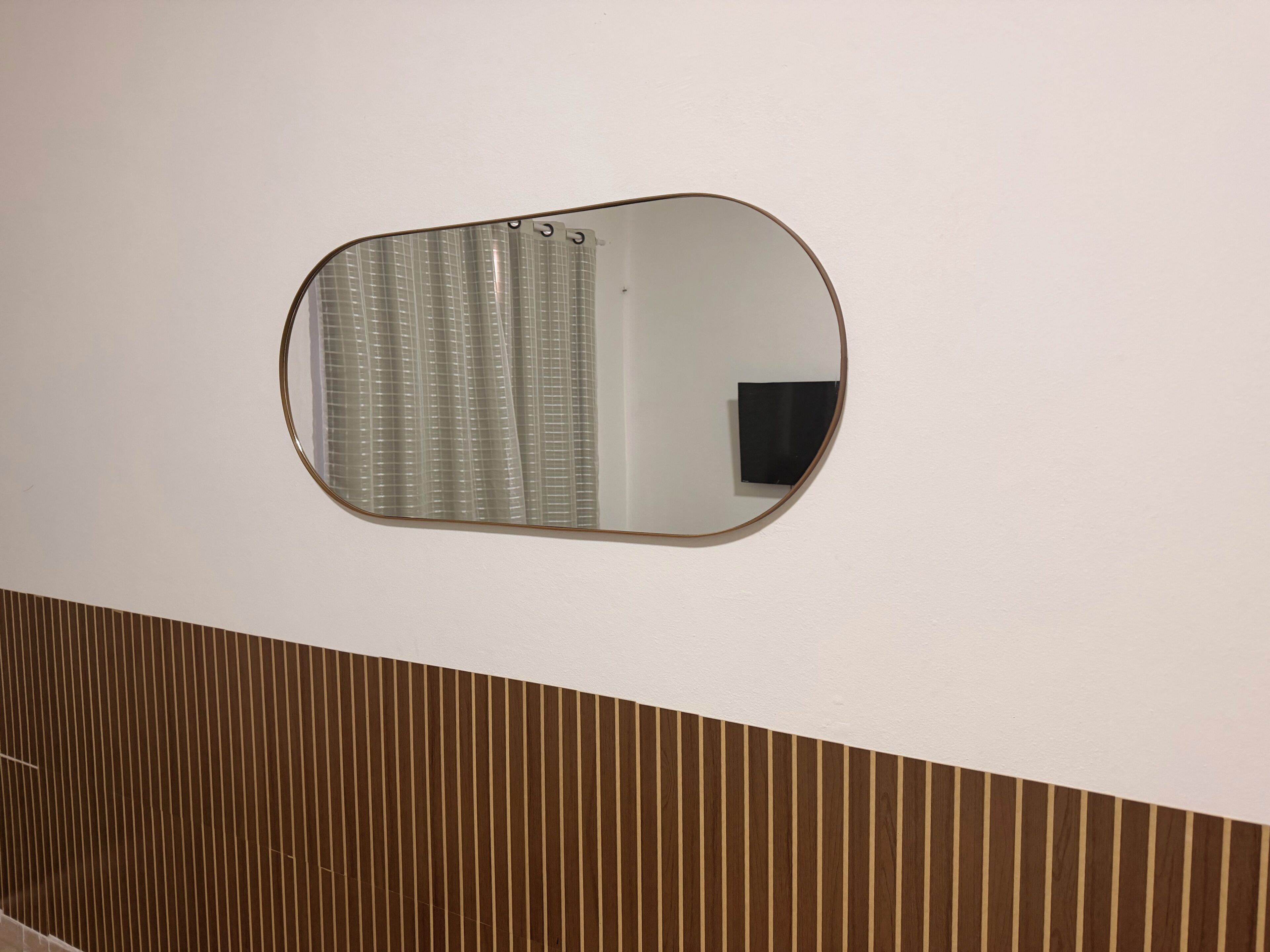 Un miroir accroché au mur, avec un panneau en bois en dessous.
