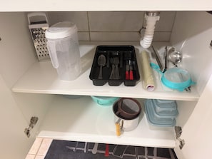 A kitchen shelf with a water dispenser, a grater, a black utensil holder, a blue strainer, and a pot.