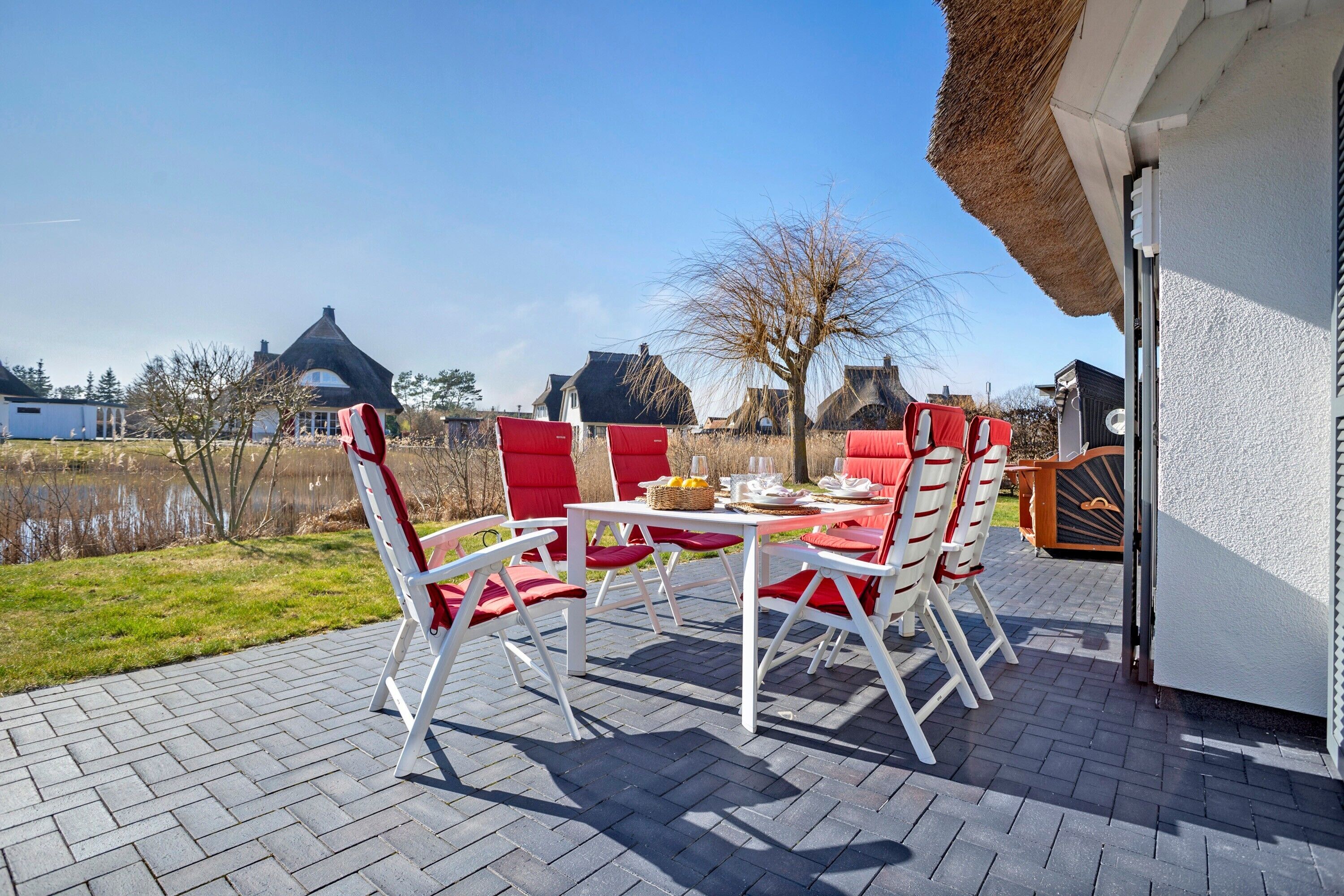 Une terrasse avec une table et des chaises, un toit de chaume et une vue sur des maisons et une étendue d’eau.