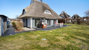 A house with a thatched roof, a patio with outdoor furniture, and a clear sky. - Holiday Home 'Idyllisches Reethaus in Strandnähe' with Shared Terrace, Private Garden and Wi-Fi (Fuhlendorf)