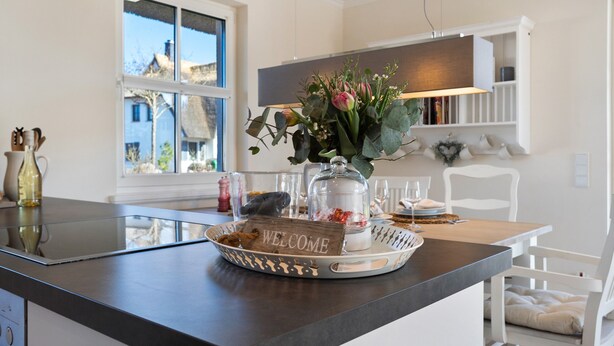 A modern kitchen with a 'WELCOME' sign, a glass-top island, and a view of the outside. - Holiday Home 'Idyllisches Reethaus in Strandnähe' with Shared Terrace, Private Garden and Wi-Fi (Fuhlendorf)