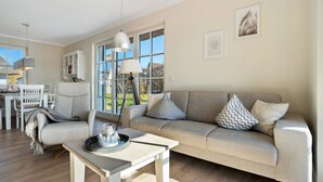 A modern living room with a sofa, a coffee table, and a dining area with a white table and chairs. - Holiday Home 'Idyllisches Reethaus in Strandnähe' with Shared Terrace, Private Garden and Wi-Fi (Fuhlendorf)