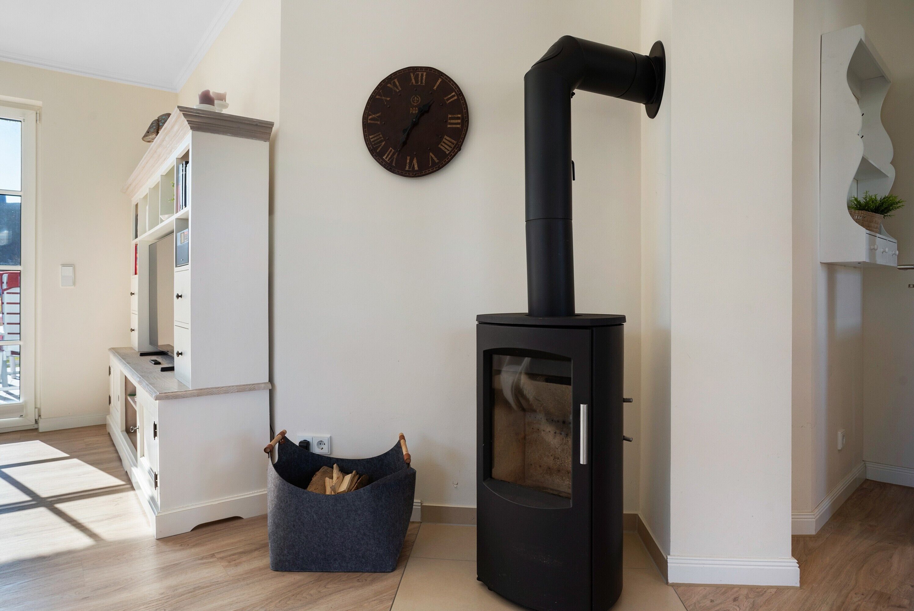 A room with a black wood-burning stove, a white cabinet, a clock, and a window.