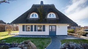 A house with a thatched roof, a front door, and a paved driveway. - Holiday Home 'Idyllisches Reethaus in Strandnähe' with Shared Terrace, Private Garden and Wi-Fi (Fuhlendorf)