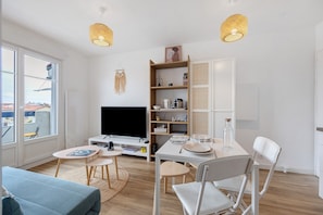 Ein modernes Wohnzimmer mit Flachbildfernseher, Esstisch mit Stühlen, Bücherregal und großem Fenster mit Aussicht.