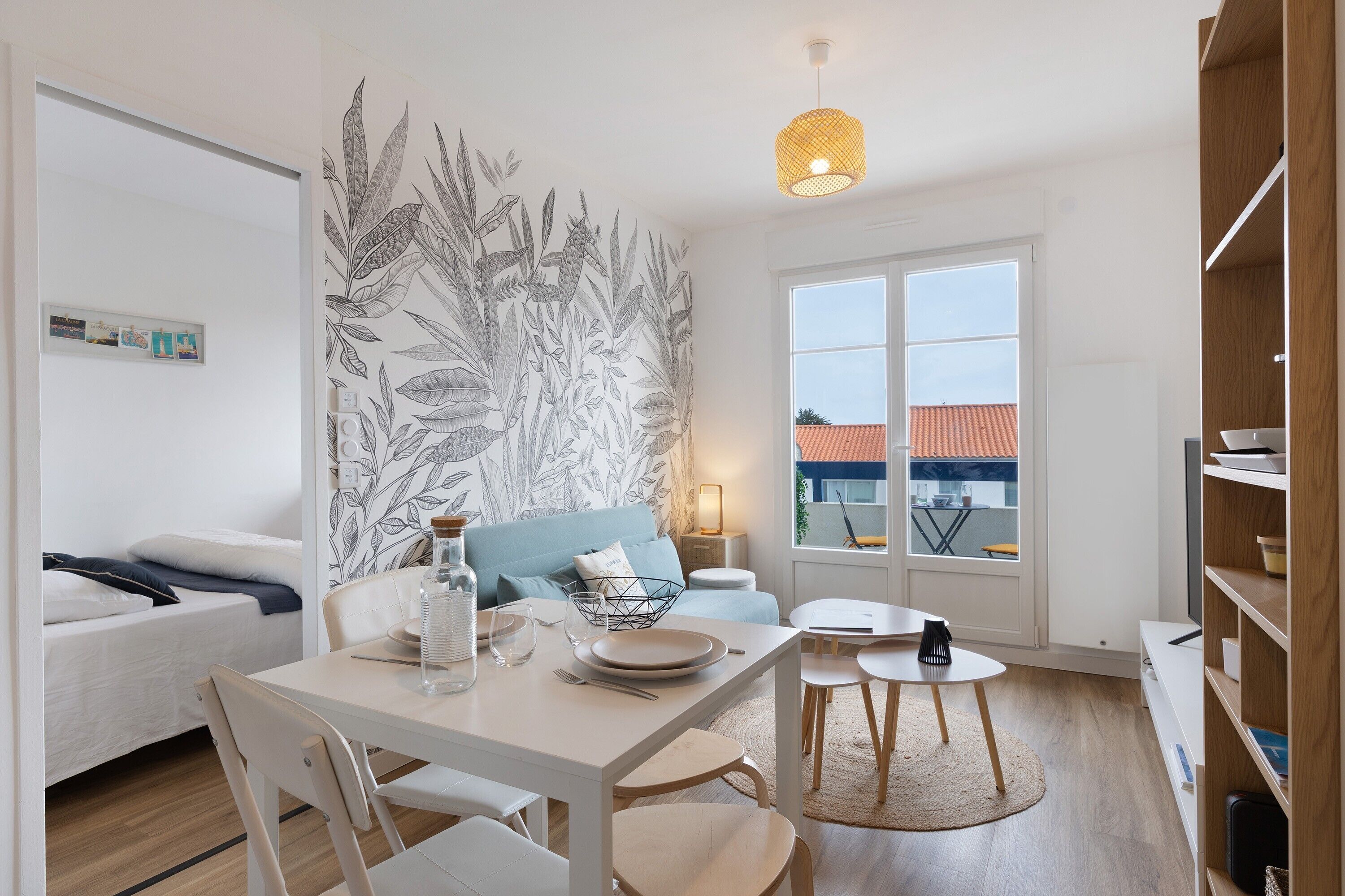Un salon moderne comprenant un coin repas, un canapé, une table basse, une lampe et une grande fenêtre donnant sur des immeubles.