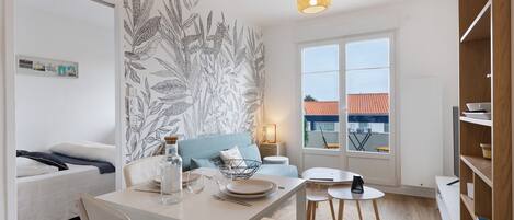 Un salon moderne comprenant un coin repas, un canapé, une table basse, une lampe et une grande fenêtre donnant sur des immeubles.