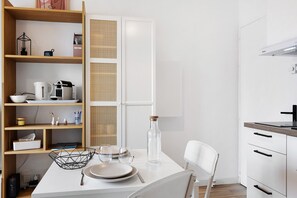 A modern kitchen with white cabinetry, a dining table with plates and glasses, a coffee maker, and a wicker basket.
