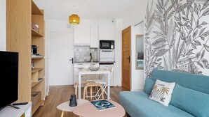 Un salon moderne comprenant un canapé, un téléviseur, un coin repas avec des chaises et une cuisine équipée.