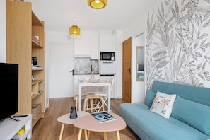A modern living room with a sofa, a TV, a dining area with chairs, and a kitchen with appliances.