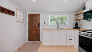 Una cocina moderna con armarios blancos, encimera de madera, horno empotrado y ventana con vistas a la vegetación.