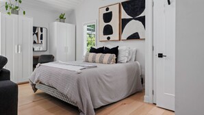 Un dormitorio con cama, armario blanco y una obra de arte en la pared.