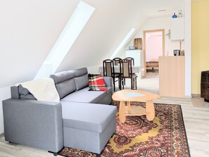 Ein modernes Loft-Apartment mit grauem Sofa, einem kleinen Holztisch, einem gemusterten Teppich und einem Essbereich mit Stühlen und Tisch.
