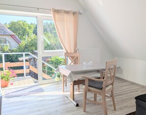 Een kamer met een houten tafel en stoelen, een raam met gordijnen en uitzicht op een tuin.