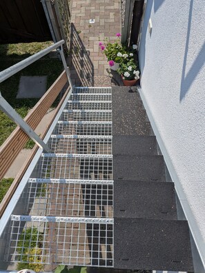 A set of outdoor stairs with metal railings, a wooden handrail, and a potted plant with flowers. - Apartment Morgensonne with Garden Access and Wi-Fi (Fuhlendorf)