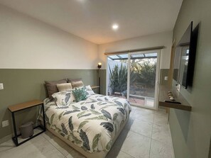 A bedroom with a bed, a nightstand, a wall-mounted TV, and a sliding glass door leading to a balcony.