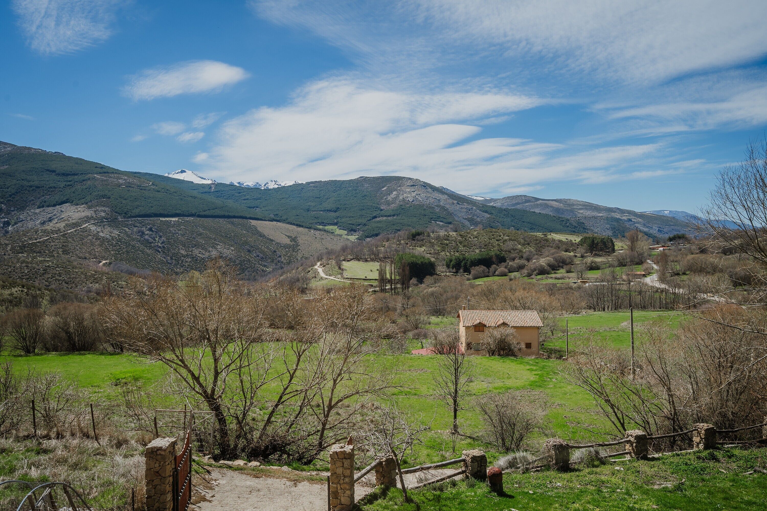 A rural landscape with a stone pathway, a small stone building, and distant mountains under a clear sky.