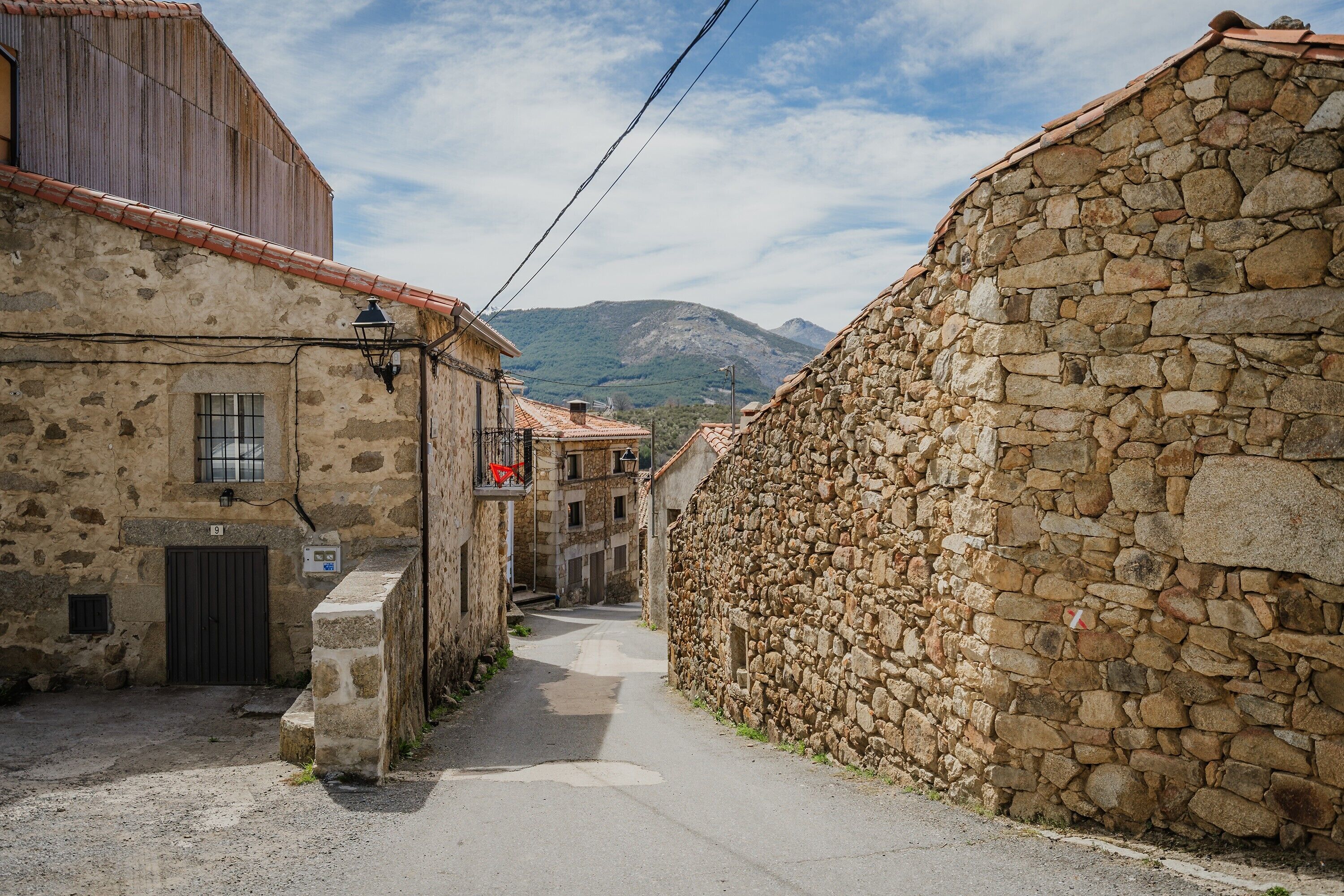 Eine enge Straße mit Steinhäusern, einer sichtbaren Tür und einem Berg im Hintergrund.
