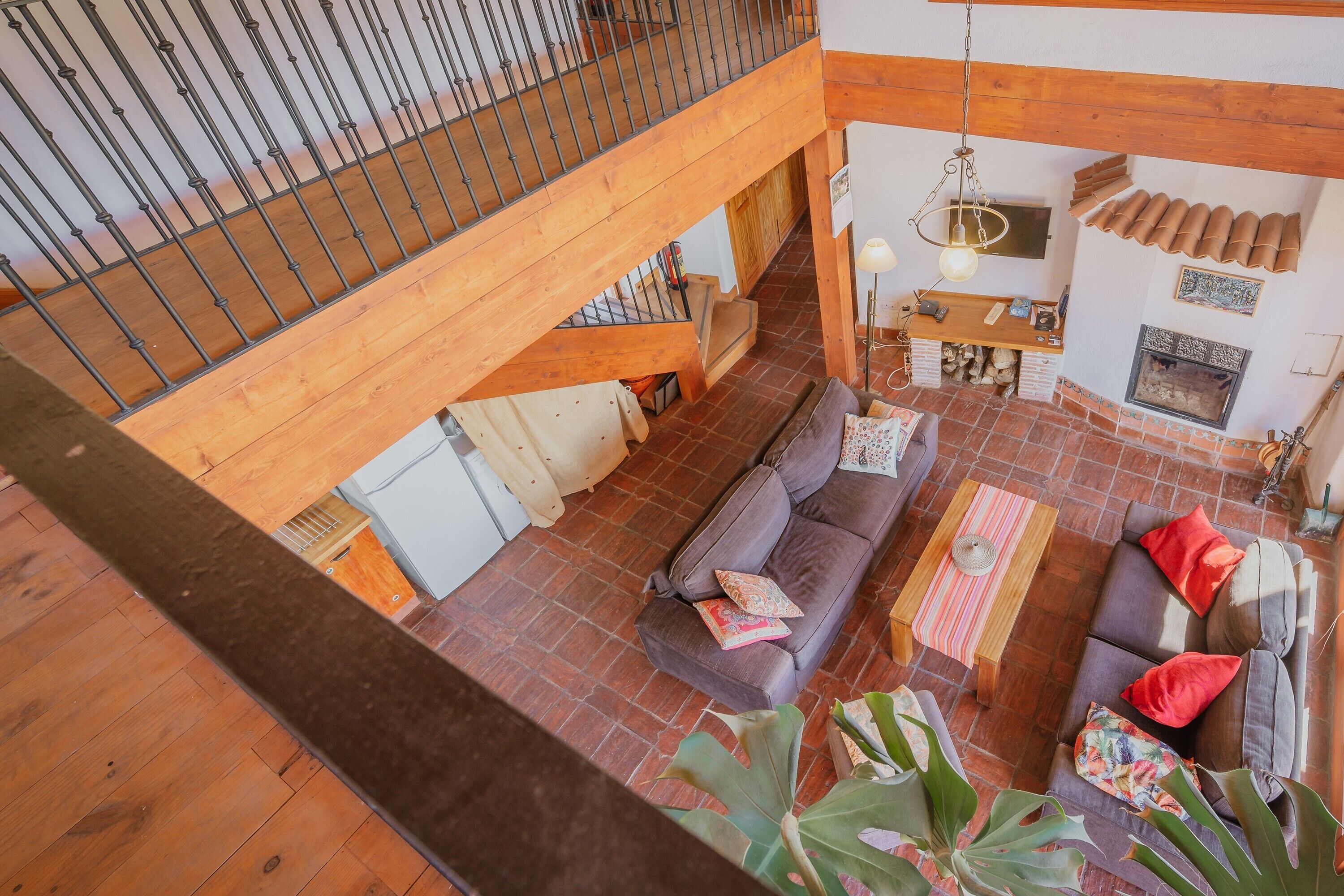 A spacious living area with a wooden staircase, a fireplace, and a high ceiling.