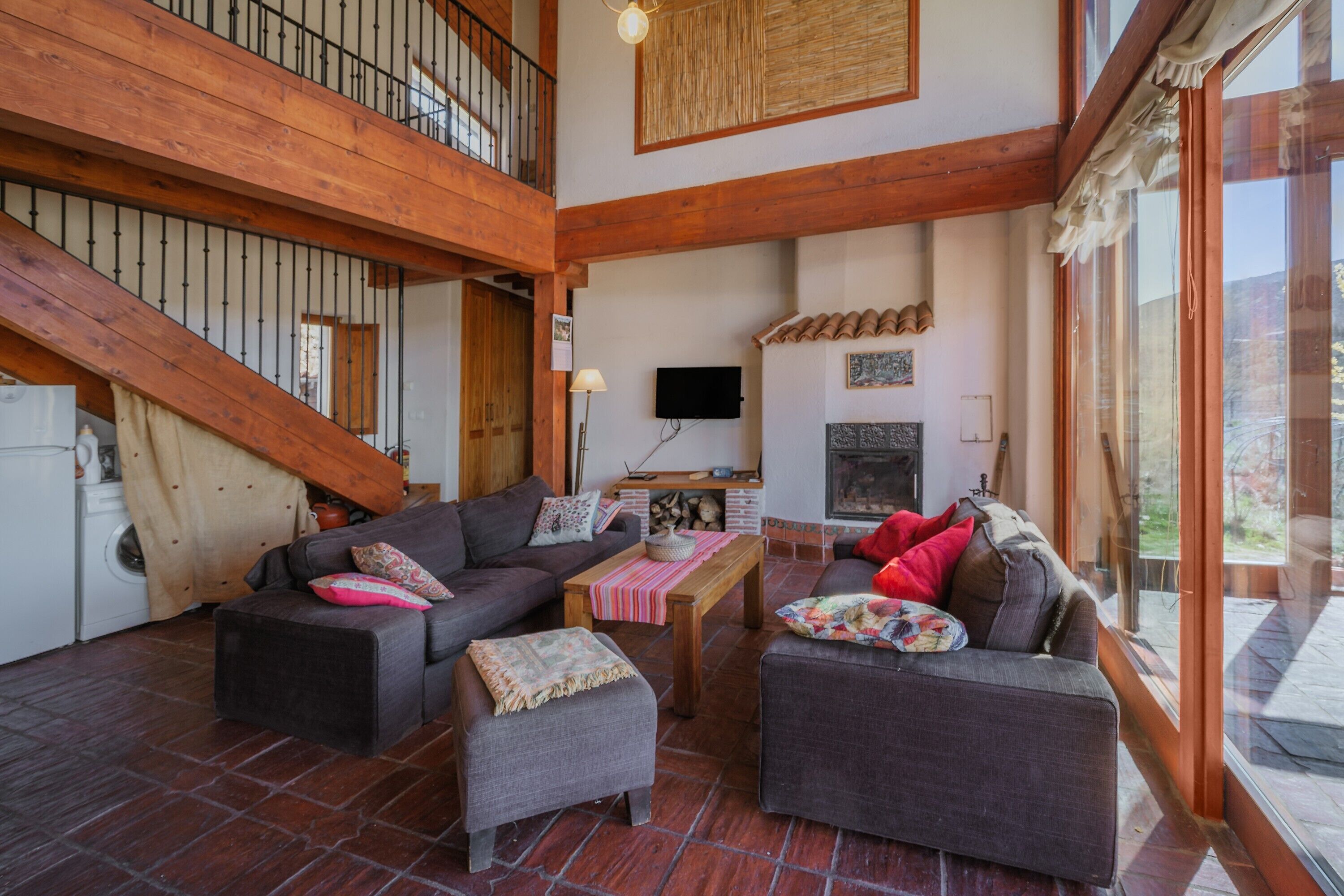 Amplia sala de estar con techo alto, vigas de madera, chimenea y un ventanal grande.