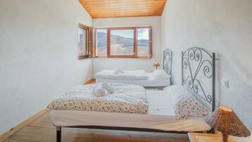 Une chambre avec un plafond en bois, un lit recouvert d’une literie à motifs floraux, une table de chevet avec une lampe, et une vue sur l’extérieur par une fenêtre.