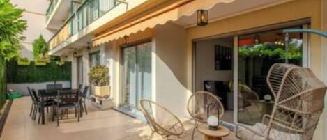 A modern outdoor patio with a dining area, wicker chairs, and a glass door leading to a covered space.