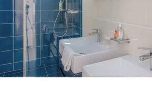 Casa de banho com azulejos azuis, cabine de chuveiro em vidro, lavatório branco e espelho.