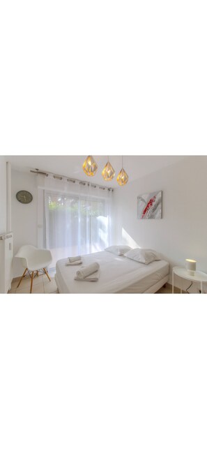 A modern bedroom with a bed, a chair, a bedside table, and a window with sheer curtains. - 3 bedrooms apartment with Terrace in Antibes for 8 people plus 2 parking spots (Antibes)