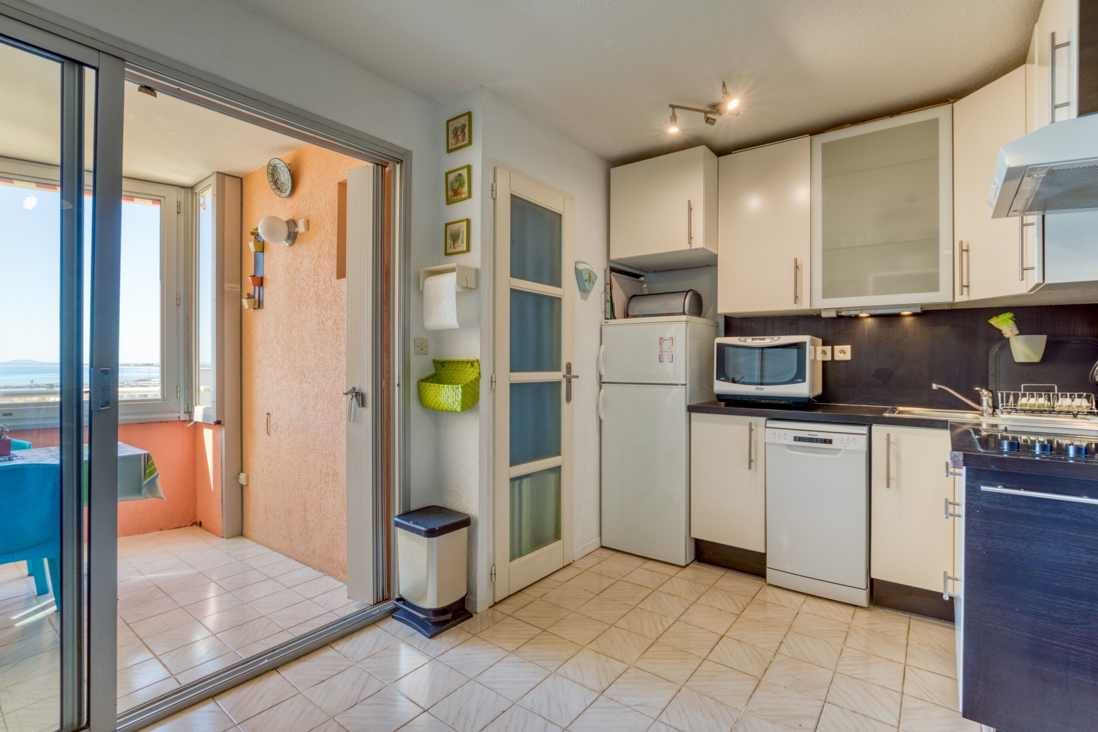 Una cocina moderna con microondas, lavavajillas y vistas a un balcón exterior a través de un ventanal.