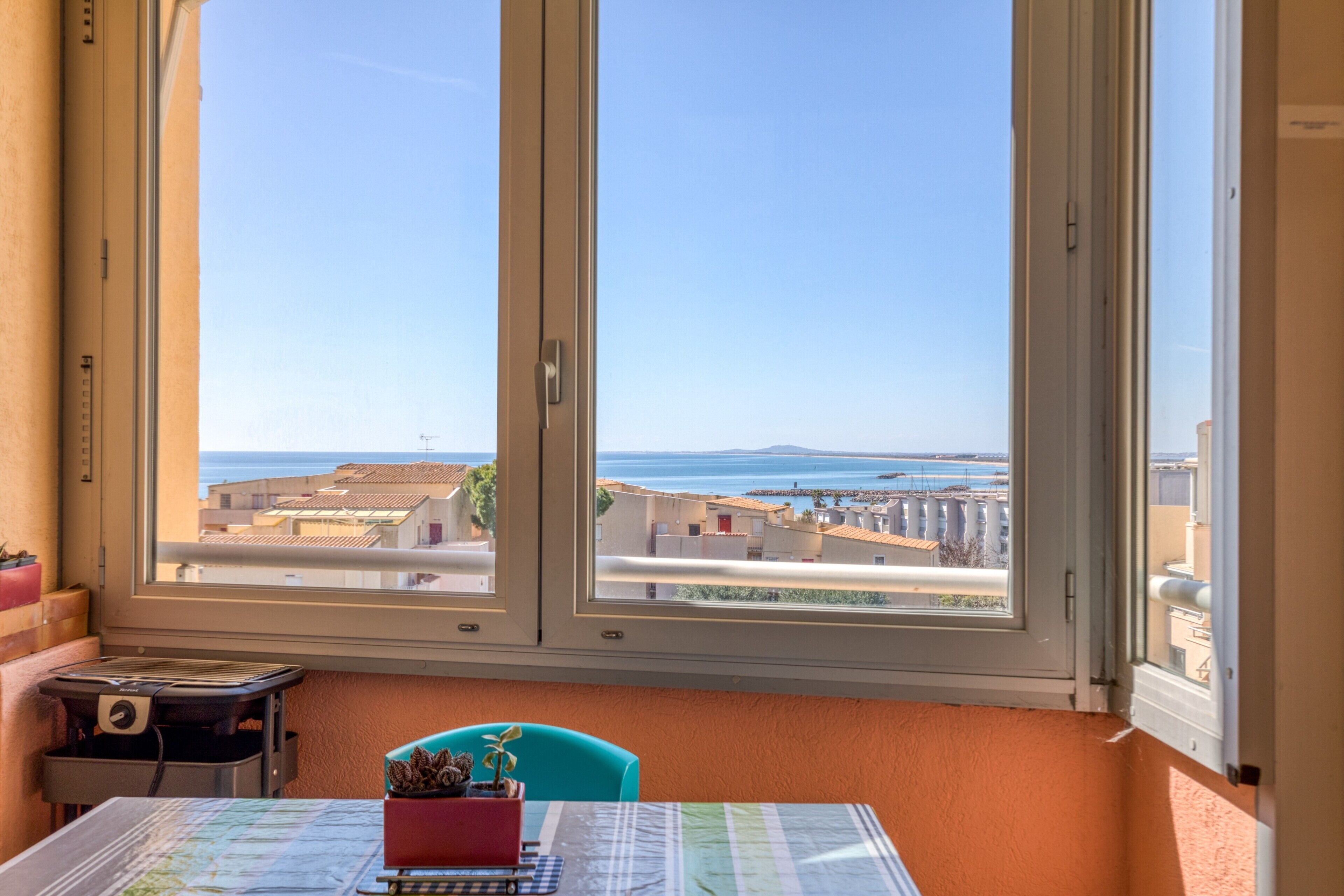 Una habitación con un ventanal grande, una mesa con un mapa, una silla y una pequeña mesa con una planta.