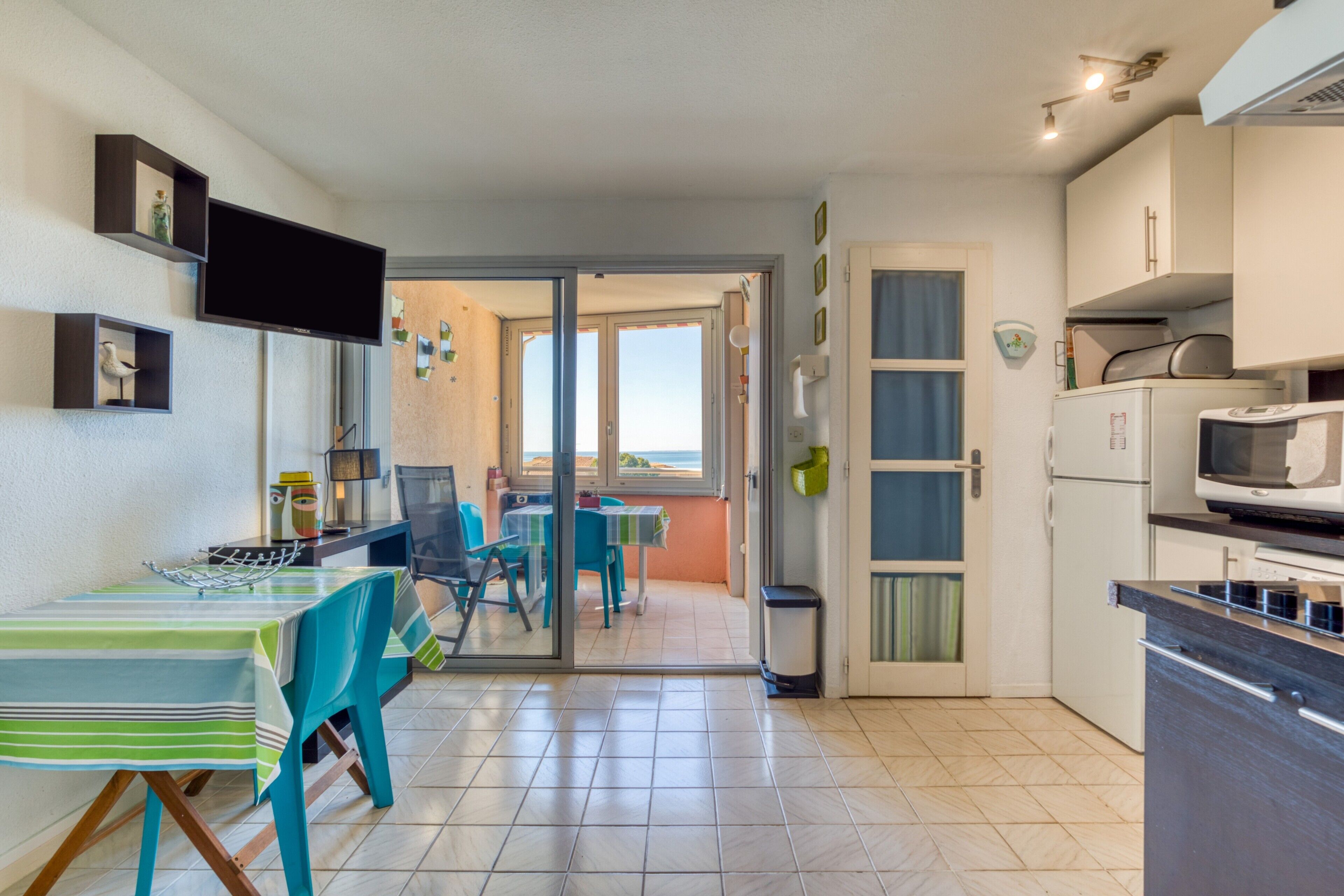 Una cocina con comedor, televisor y vista por un ventanal.