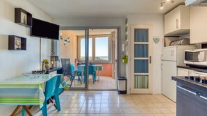 Une cuisine avec un coin repas, un téléviseur et une vue sur l’extérieur grâce à une porte vitrée.
