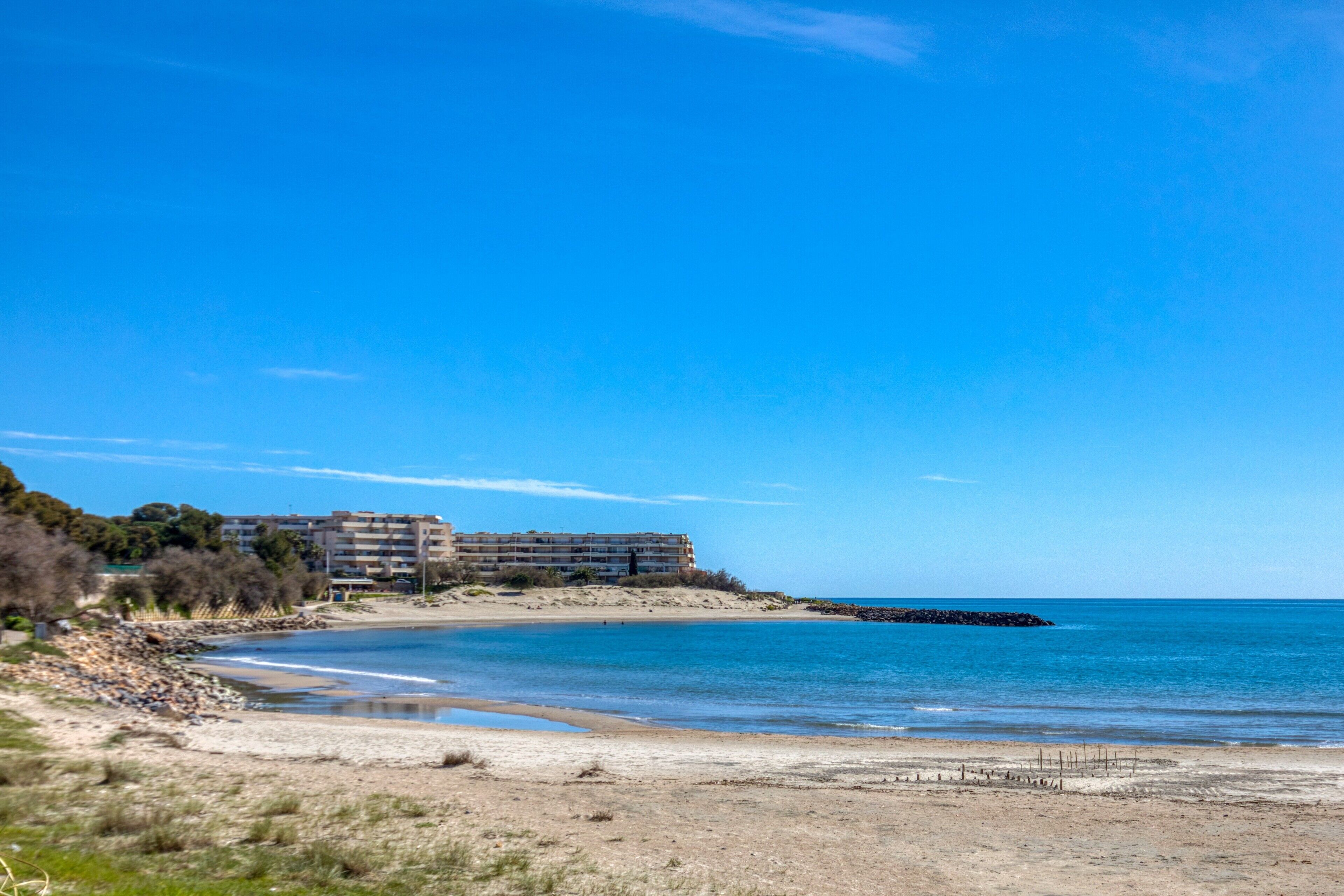 Un hotel frente al mar con vista a la playa, un litoral rocoso y un cielo azul despejado.
