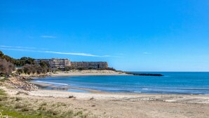 Un hôtel en bord de mer offrant une vue sur la plage, avec un littoral rocheux et un ciel bleu dégagé.