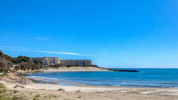 Un hotel frente al mar con vista a la playa, un litoral rocoso y un cielo azul despejado.