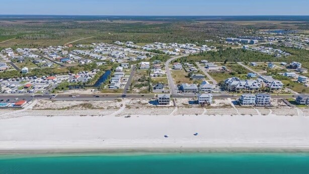 Vista aérea de un pueblo costero con edificios residenciales, una playa y una carretera que conduce a la costa.