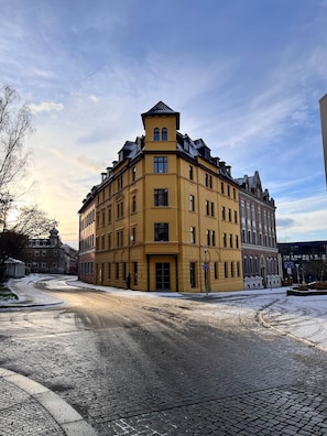 Um edifício de esquina com fachada amarela, várias janelas e um estilo arquitetônico marcante.