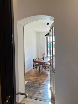 Uma sala de jantar com mesa e cadeiras de madeira, um vaso com flores e um lustre.