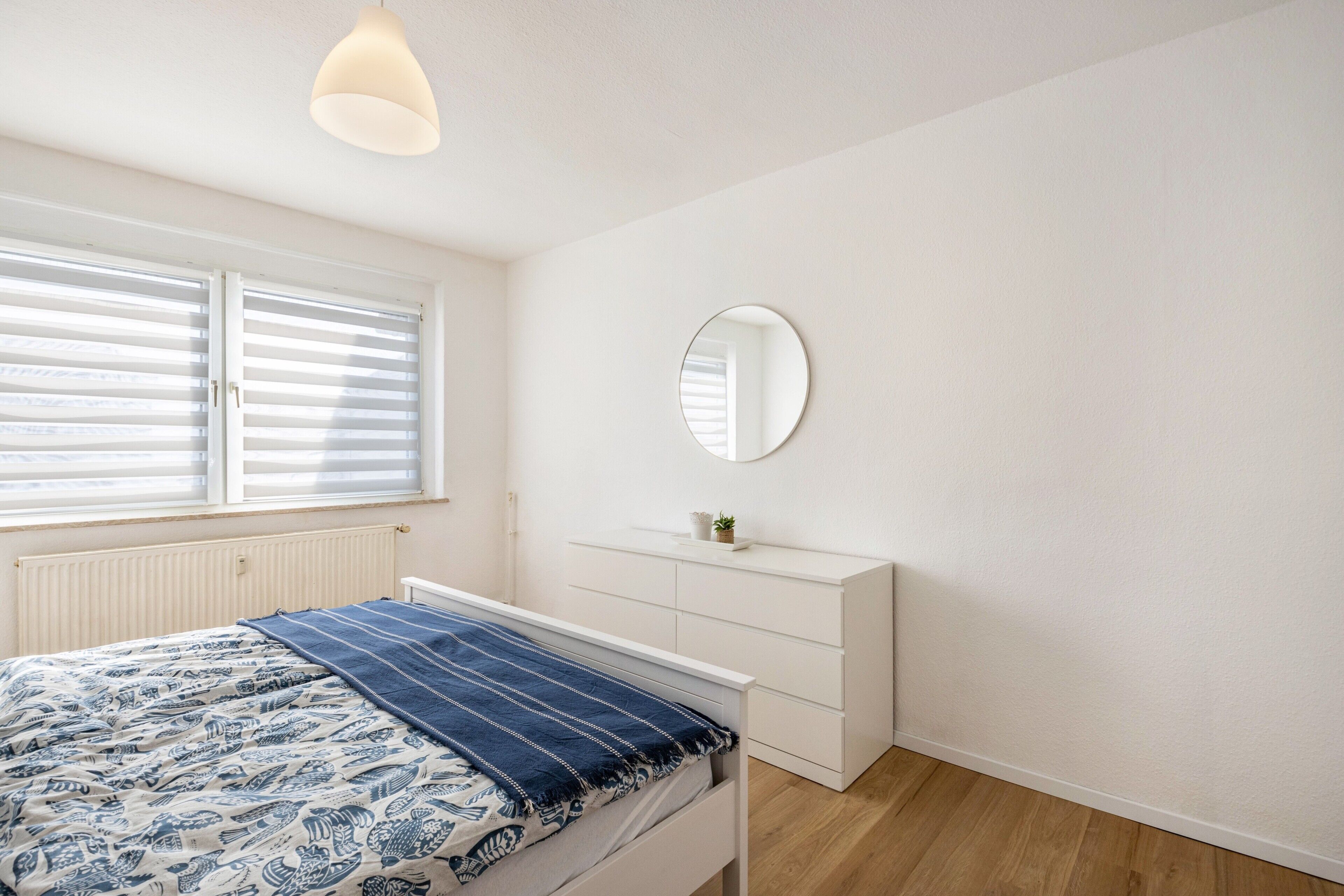 Ein Schlafzimmer mit einem Bett, einem Schminktisch, einem Spiegel und einem Fenster mit Jalousien.