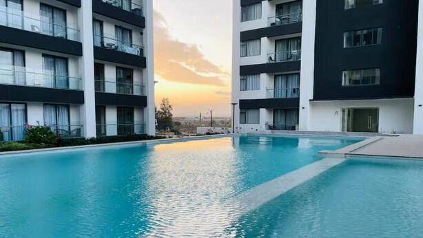 A swimming pool surrounded by modern apartment buildings with balconies, during sunset. - 1BR Luxury Suites near Airport with pool/gym/Cityview (Nairobi)