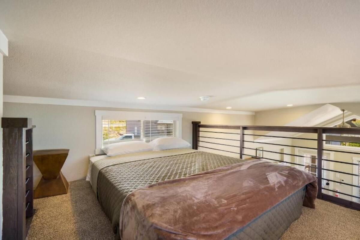A bedroom with a bed, a window, a nightstand, and a balcony with a railing.