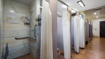 A row of white shower stalls with glass doors, a handrail, and a marble wall.