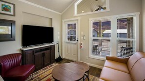A living room with a flat-screen TV, a red leather chair, a brown leather couch, a small round table, and a window with blinds. - HTR Moab (Moab)