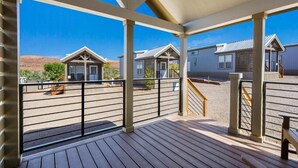 A covered outdoor area with a wooden deck, metal railing, and a view of multiple buildings in the background. - HTR Moab (Moab)