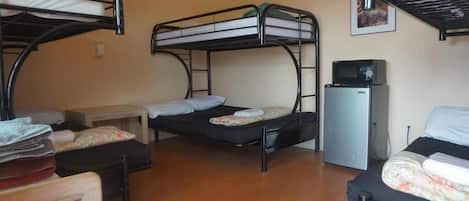 A dormitory room with bunk beds, a small desk, a microwave, and a chair.