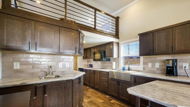 A kitchen with dark wood cabinets, a marble countertop, and a built-in microwave. - HTR Moab (Moab)