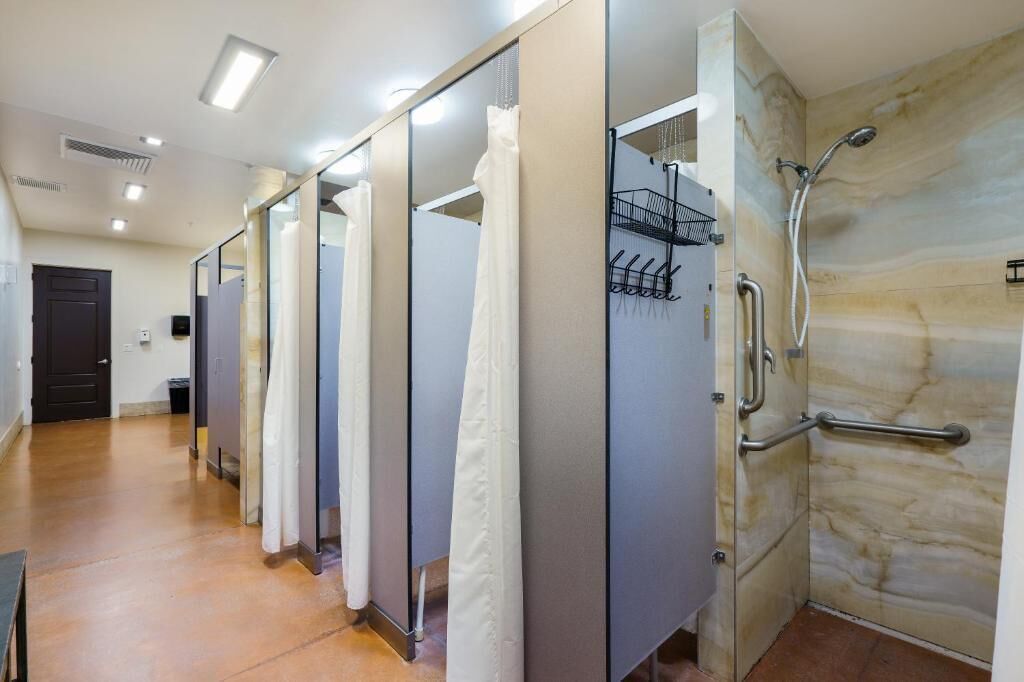 Uma fileira de cabines de chuveiro individuais com portas de vidro, um secador de mãos e um porta-toalhas.